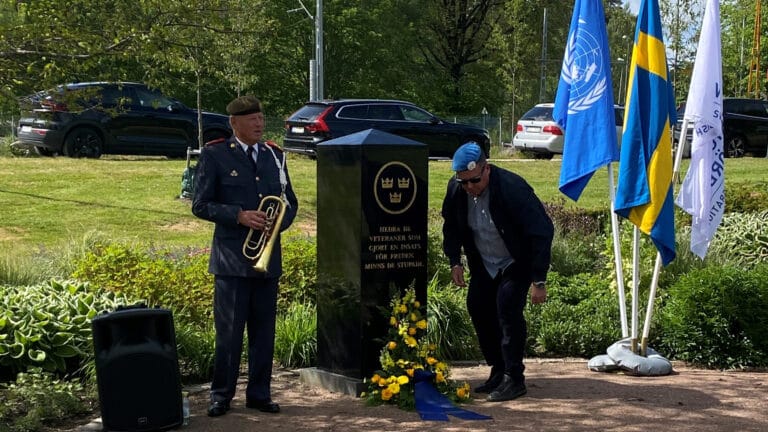 Två män, en håller i en trumpet och en lägger ner blommor vid en minnessten.